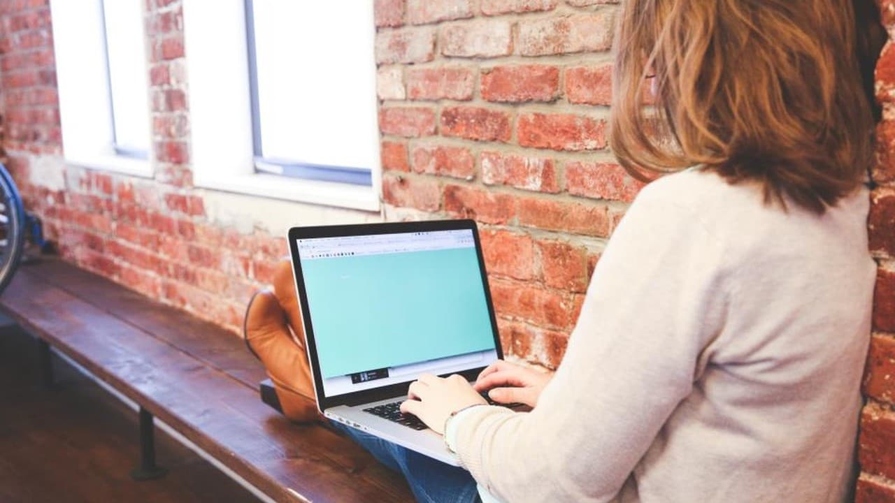 Woman working on a laptop in a bright brick-walled workspace